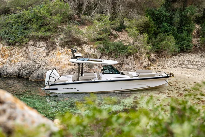 The Image of 2026 Axopar 29 Sun-Top boat anchored near rocky shoreline with lush greenery. - 0
