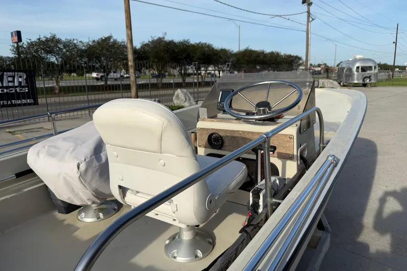 Slide: The Image of 1983 Boston Whaler Sport 15 boat interior with steering wheel and seating, parked outdoors. - 6