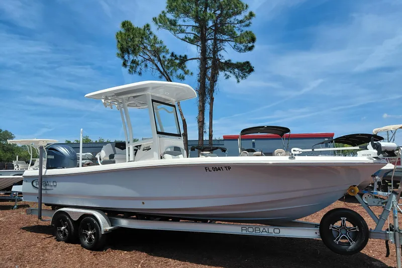 The Image of 2023 Robalo 246 Cayman boat on trailer, parked outdoors under clear blue sky. - 1