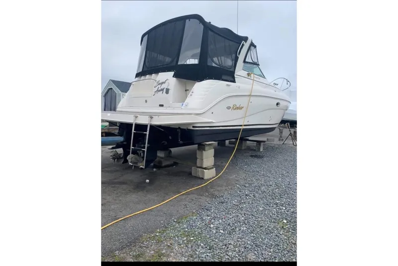 The Image of 2005 Rinker Fiesta Vee 320 boat on blocks, with black canopy, in a gravel yard. - 0