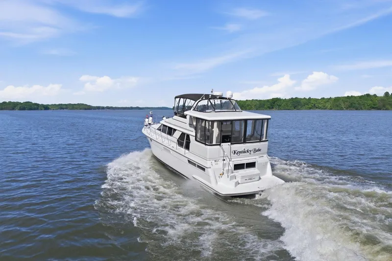 Slide: The Image of 1998 Carver 445 Aft Cabin Motor Yacht cruising on a serene lake under a clear sky. - 3