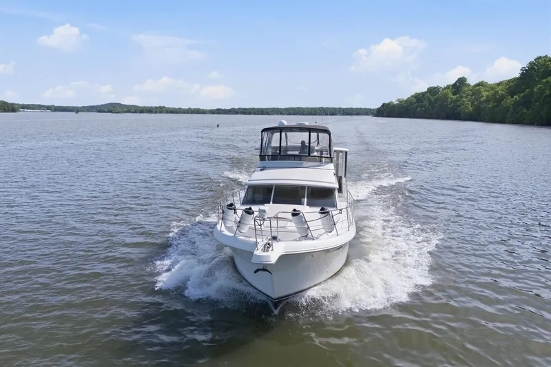Slide: The Image of 1998 Carver 445 Aft Cabin Motor Yacht cruising on a serene lake under a clear sky. - 5