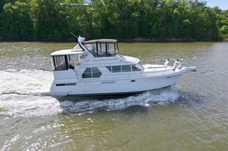Slide: The Image of 1998 Carver 445 Aft Cabin Motor Yacht cruising on a river with lush green backdrop. - 6