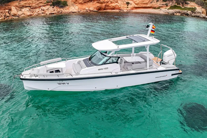 Slide: The Image of 2026 Axopar 29 Sun-Top boat on clear turquoise water near rocky shoreline. - 2
