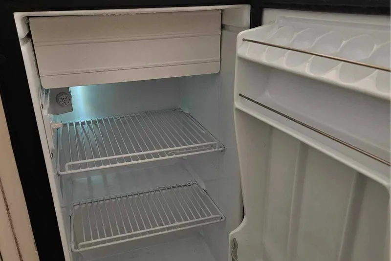 Slide: The Image of Empty refrigerator inside a 1998 Tiara Yachts 3500 Open, featuring wire shelves and door storage. - 24