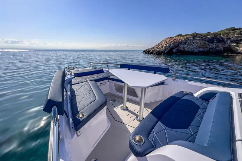 Slide: The Image of 2026 Axopar 29 XC Cross Cabin boat with blue seating, table, and scenic ocean view. - 10