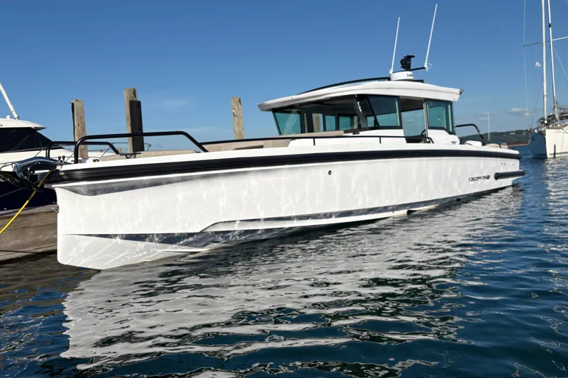 Slide: The Image of 2026 Axopar 37 XC Cross Cabin boat docked on calm water under clear blue sky. - 2