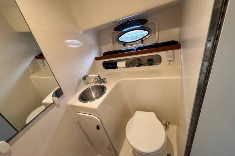 Slide: The Image of Compact bathroom in 1993 Tiara Yachts 3100 Open, featuring sink, toilet, and porthole window. - 25