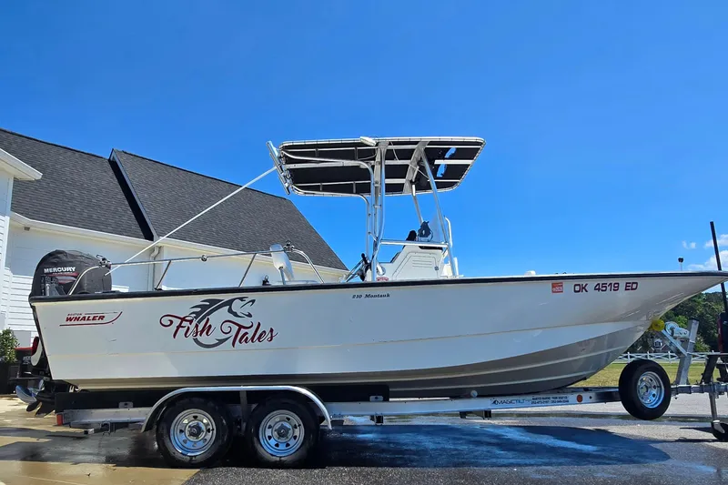 The Image of 2017 Boston Whaler 210 Montauk boat on trailer, labeled "Fish Tales," under clear blue sky. - 1