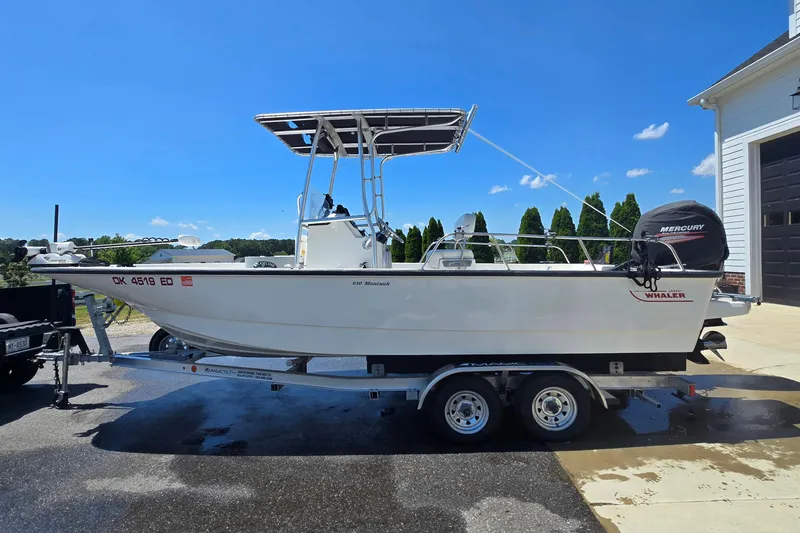 Slide: The Image of 2017 Boston Whaler 210 Montauk boat on trailer, parked outdoors under clear blue sky. - 4