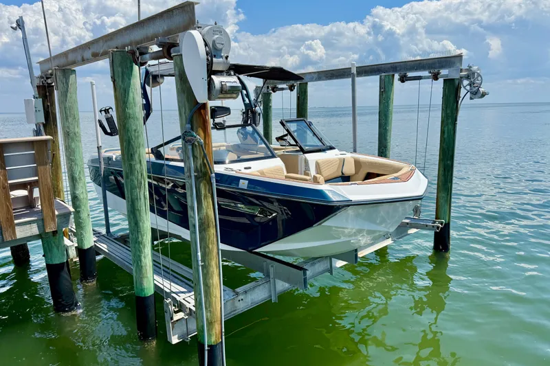 Slide: The Image of 2021 Nautique Super Air Nautique G21 boat on lift over water, under a cloudy sky. - 6