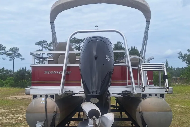 Slide: The Image of 2021 Ranger Reata 200F pontoon boat with outboard motor, parked on grassy area. - 4