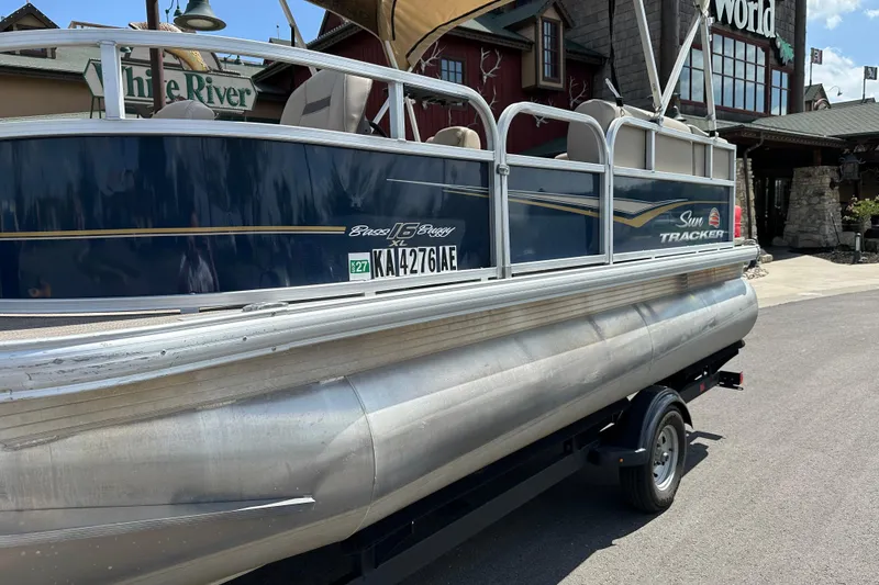 Slide: The Image of 2024 Sun Tracker Bass Buggy 16 XL Select pontoon boat on trailer, parked outdoors. - 16