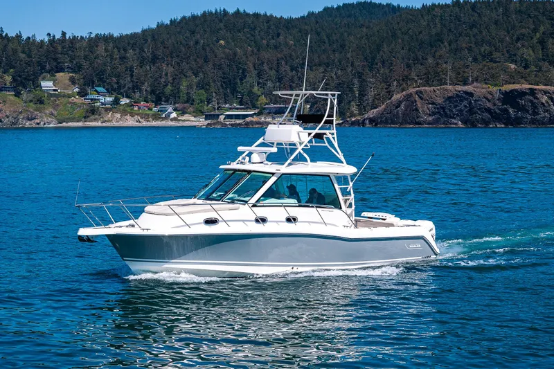 The Image of 2019 Boston Whaler 345 Conquest cruising on a scenic blue lake with forested hills. - 0