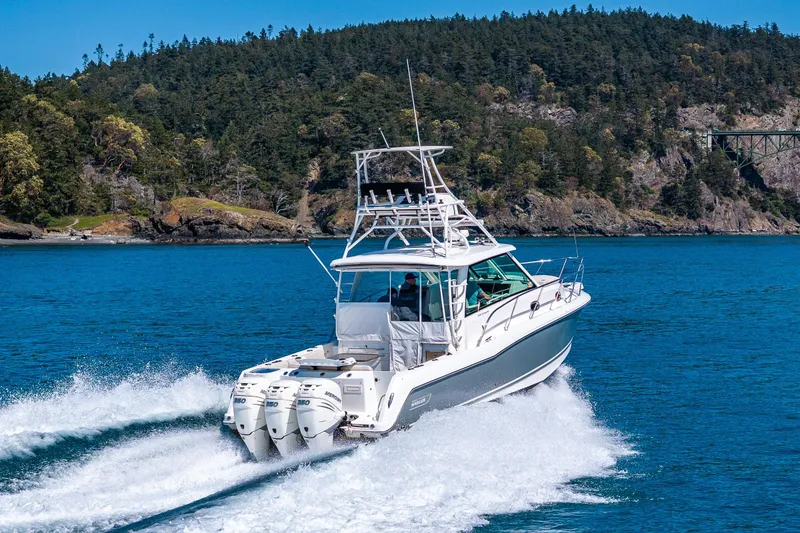 Slide: The Image of 2019 Boston Whaler 345 Conquest cruising on blue water near forested shoreline. - 2