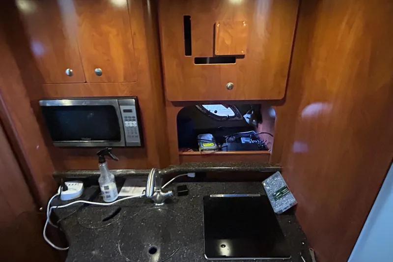 Slide: The Image of 2013 Rinker 310 Express Cruiser kitchen with microwave, sink, and wooden cabinetry. - 17