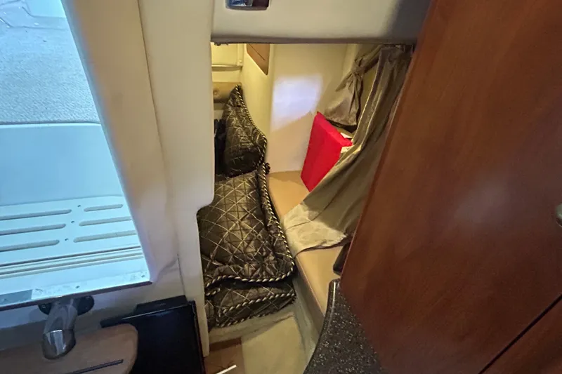 Slide: The Image of 2013 Rinker 310 Express Cruiser cabin interior with cozy bedding and wooden accents. - 58