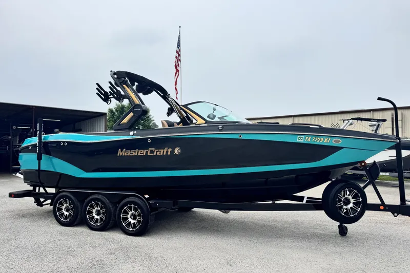 The Image of 2025 MasterCraft X26 boat on trailer, displayed outdoors with American flag in background. - 1