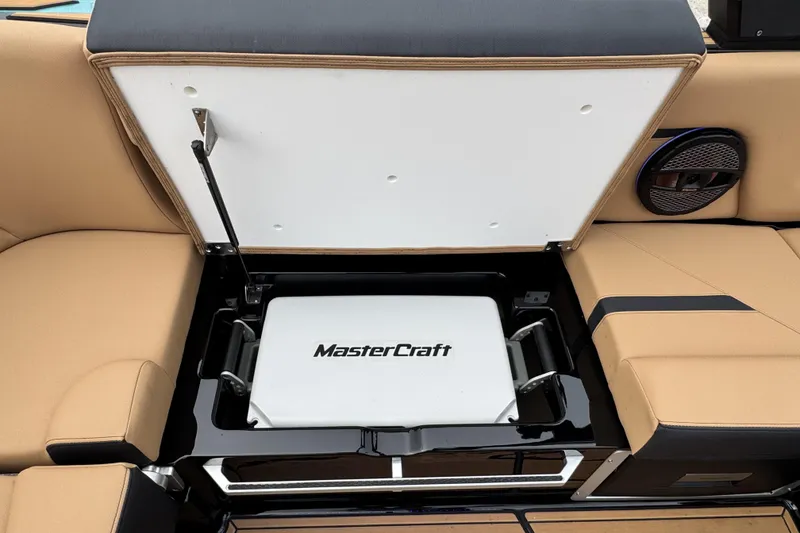 Slide: The Image of Open storage compartment in 2025 MasterCraft X26 boat, featuring beige seating and branded cooler. - 17