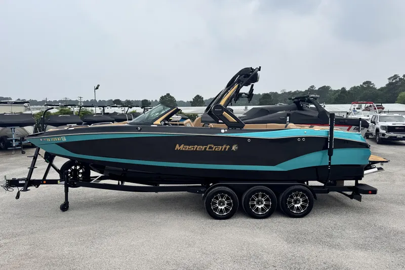 Slide: The Image of 2025 MasterCraft X26 boat on trailer, black and teal design, parked outdoors. - 6