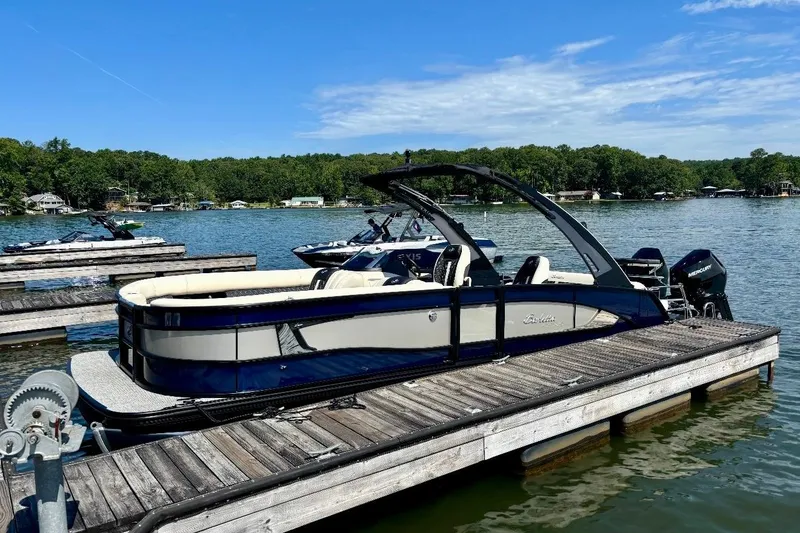 Slide: The Image of 2025 Barletta L25UCAT pontoon boat docked on a serene lake under a clear blue sky. - 3