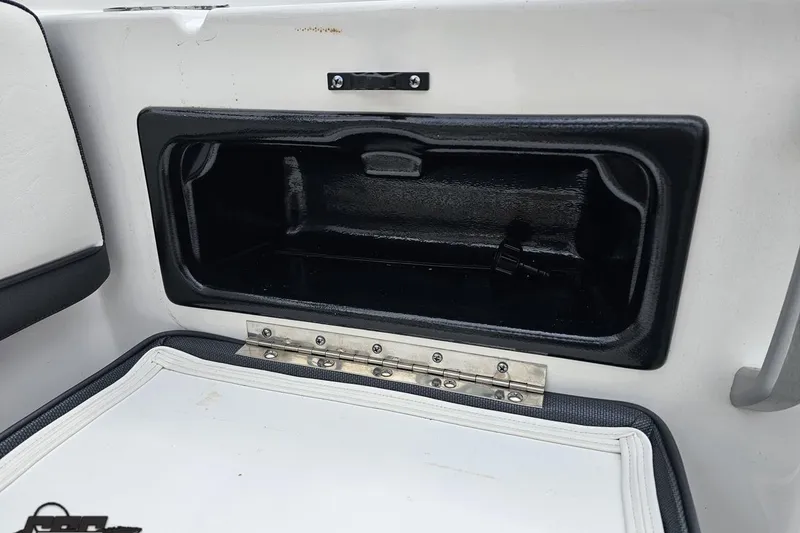 Slide: The Image of Storage compartment on a 2022 Yamaha Boats AR195, featuring a black interior and metal hinge. - 46