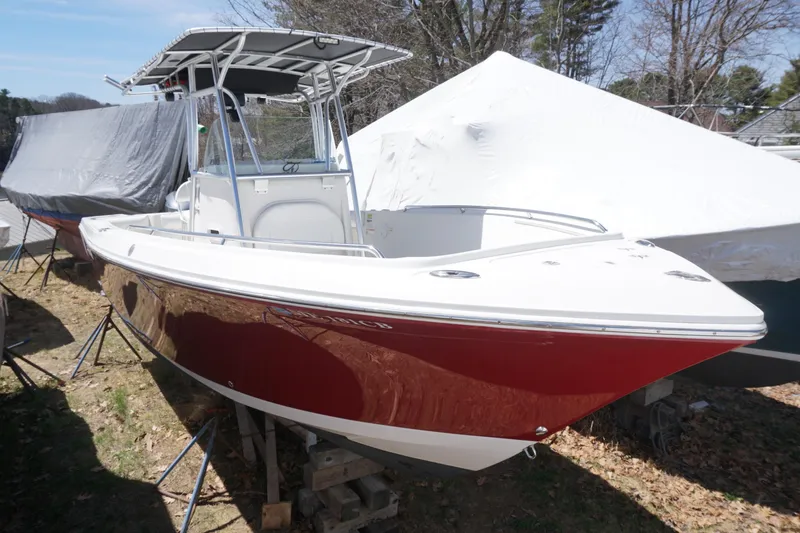 The Image of 2012 Sailfish 2380 CC boat with red hull, docked outdoors, covered boats nearby. - 1