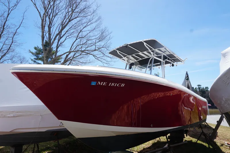 Slide: The Image of 2012 Sailfish 2380 CC boat with red hull, parked outdoors under clear sky. - 5