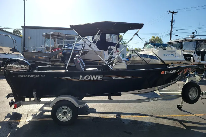 Slide: The Image of 2017 Lowe Fishing Machine 160S boat on trailer, equipped with Mercury engine, parked outdoors. - 5