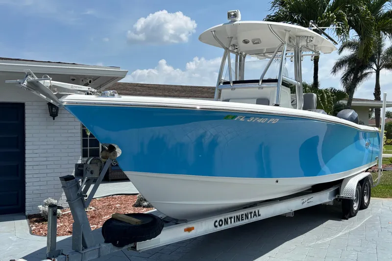 The Image of 2011 Sea Hunt Gamefish 25 boat on trailer, parked near a house with palm trees. - 0