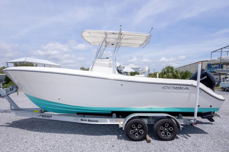 Slide: The Image of 2022 Cobia 237 Center Console boat on trailer, white and teal design, outdoor display. - 16