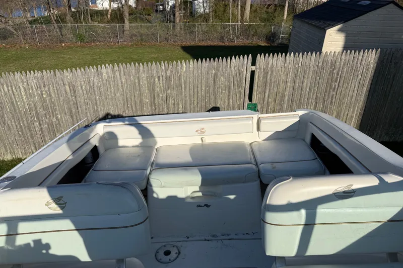 Slide: The Image of 2000 Sea Ray 215 Express Cruiser boat interior with cushioned seating, wooden fence background. - 5