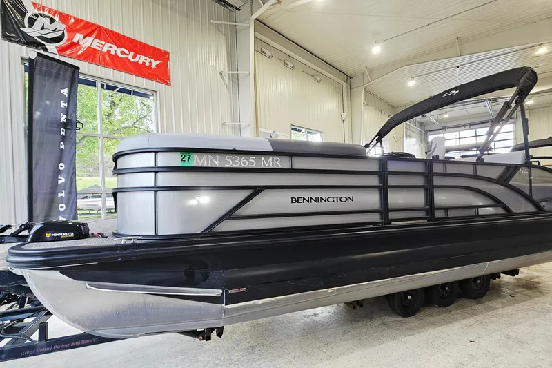 Slide: The Image of 2024 Bennington 22 S Swingback pontoon boat displayed indoors with Mercury and Volvo Penta banners. - 3