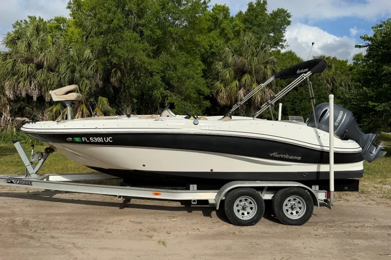 The Image of 2016 Hurricane SunDeck Sport 203 OB boat on trailer, parked outdoors with lush greenery. - 0