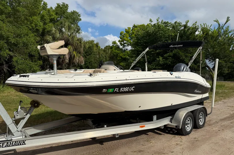 Slide: The Image of 2016 Hurricane SunDeck Sport 203 OB boat on trailer, parked outdoors with lush greenery. - 2