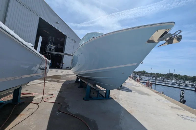 Slide: The Image of 2023 Cobia 301 Center Console boat on stands near marina and warehouse. - 30