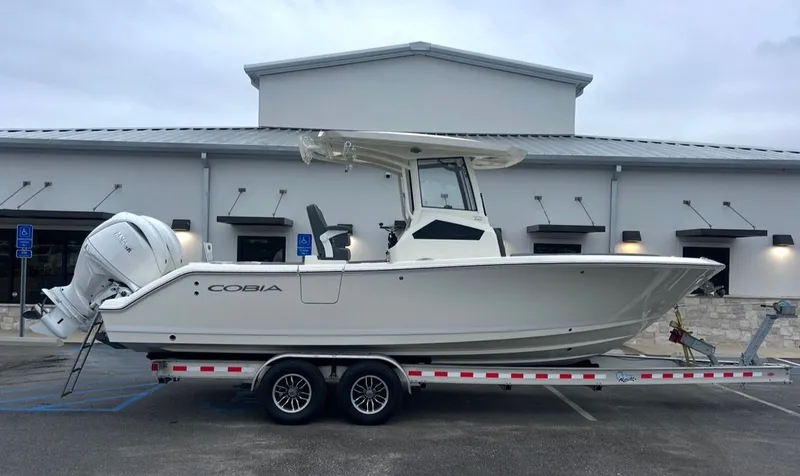 The Image of 2026 Cobia 245CC boat on trailer in front of building. - 1