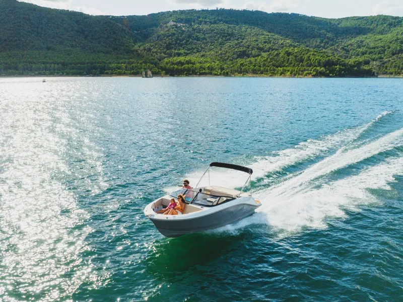 Slide: The Image of Bayliner V20i 2026 cruising on a sunny lake with green hills. - 4
