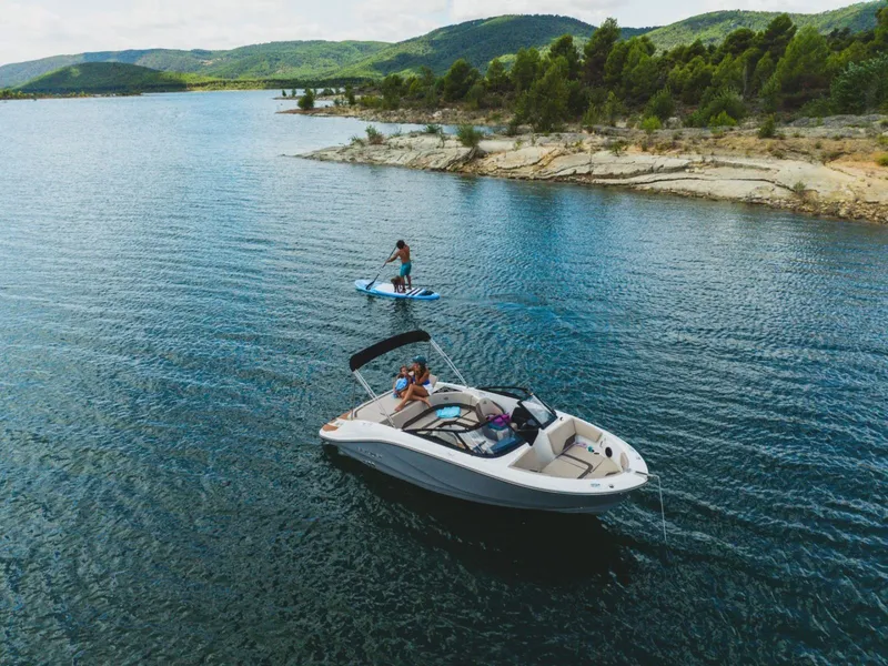 Slide: The Image of Bayliner V20i 2026 on water with paddleboarder in scenic landscape. - 7