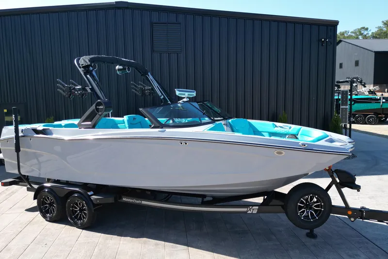 Slide: The Image of 2025 MasterCraft XT24 boat with turquoise interior on a trailer, parked outdoors. - 15