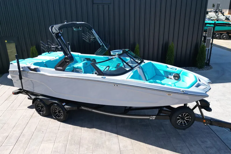 Slide: The Image of 2025 MasterCraft XT24 boat with turquoise interior on a trailer, parked outdoors. - 16