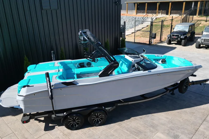 Slide: The Image of 2025 MasterCraft XT24 boat with turquoise interior on a trailer, parked outdoors. - 17