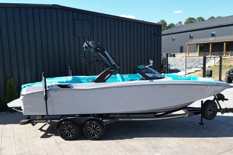 Slide: The Image of 2025 MasterCraft XT24 boat on trailer, parked outdoors near modern building. - 18
