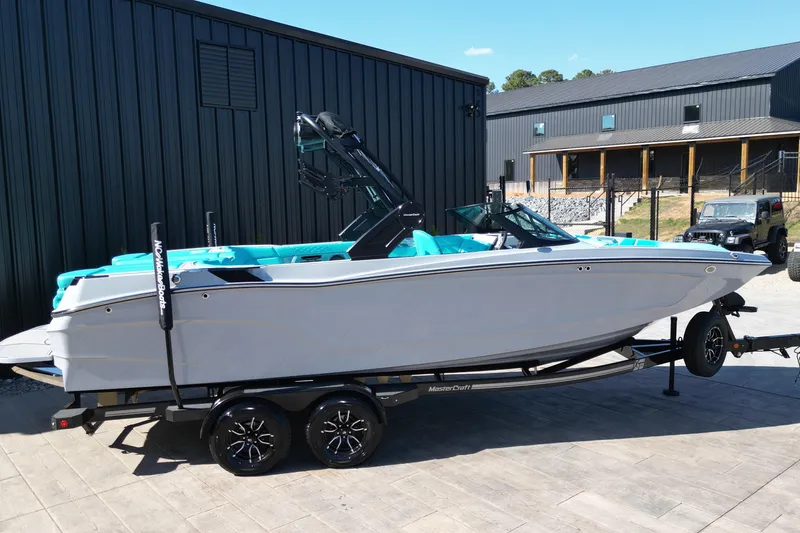 Slide: The Image of 2025 MasterCraft XT24 boat on trailer, parked outdoors near modern buildings. - 19