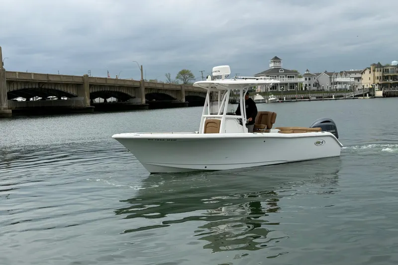 Slide: The Image of 2022 Sea Hunt Ultra 234 boat cruising near a bridge and waterfront homes. - 2