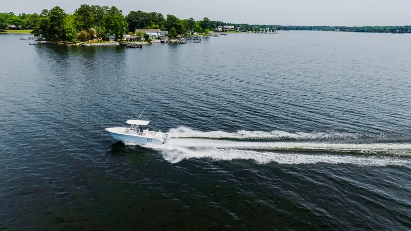 Slide: The Image of 2026 Sea Hunt Ultra 255 SE boat cruising on a serene lake with lush shoreline. - 25