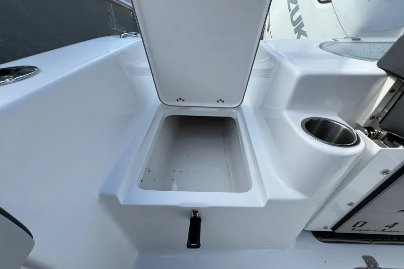 Slide: The Image of 2026 Sea Pro 240 Dual Console boat storage compartment with cup holder and Suzuki engine detail. - 25