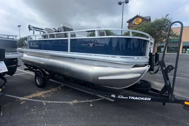 Slide: The Image of 2026 Sun Tracker Bass Buggy 18 DLX pontoon boat on trailer in parking lot. - 2