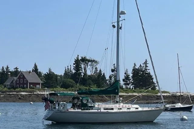 Slide: The Image of 1982 Sabre 34 sailboat anchored in scenic coastal waters with trees and house in background. - 50