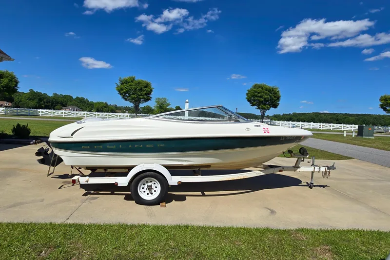 The Image of 1999 Bayliner 1850 Capri SS boat on trailer, parked outdoors under a clear blue sky. - 1